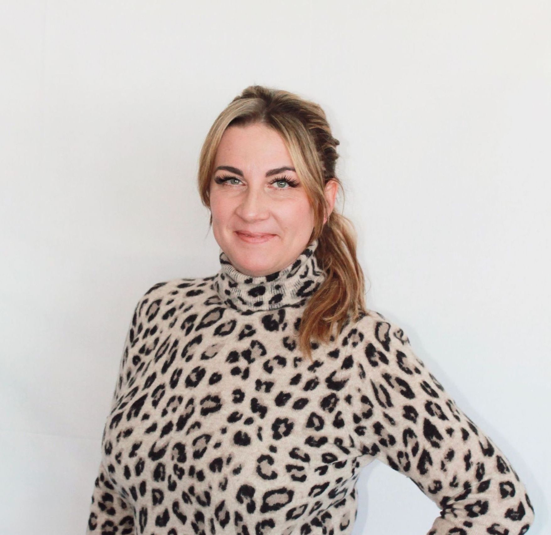 Jenna Clubine with blonde hair in a ponytail, wearing a leopard-print turtleneck, smiling at the camera.