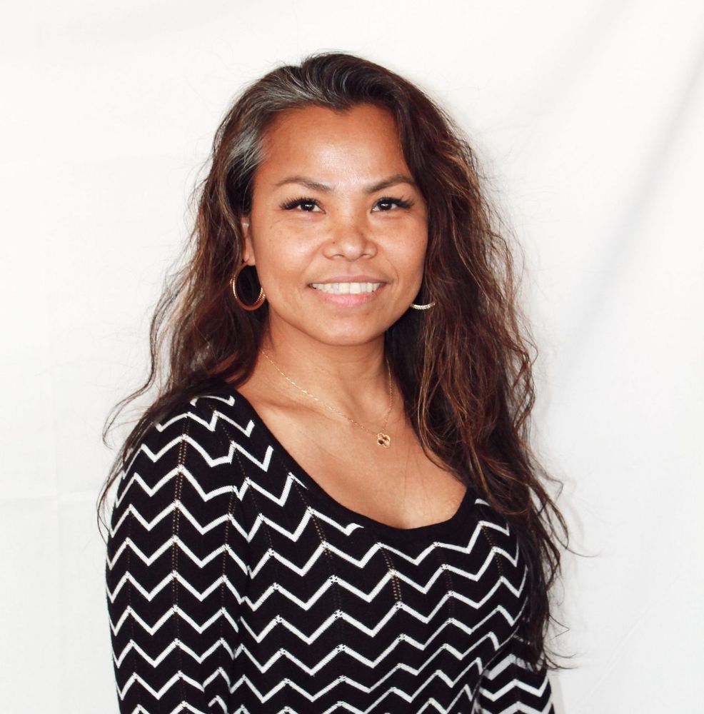 Jenny Stevenson with long brown hair, smiling, wearing a black and white zig-zag top and gold hoop earrings.