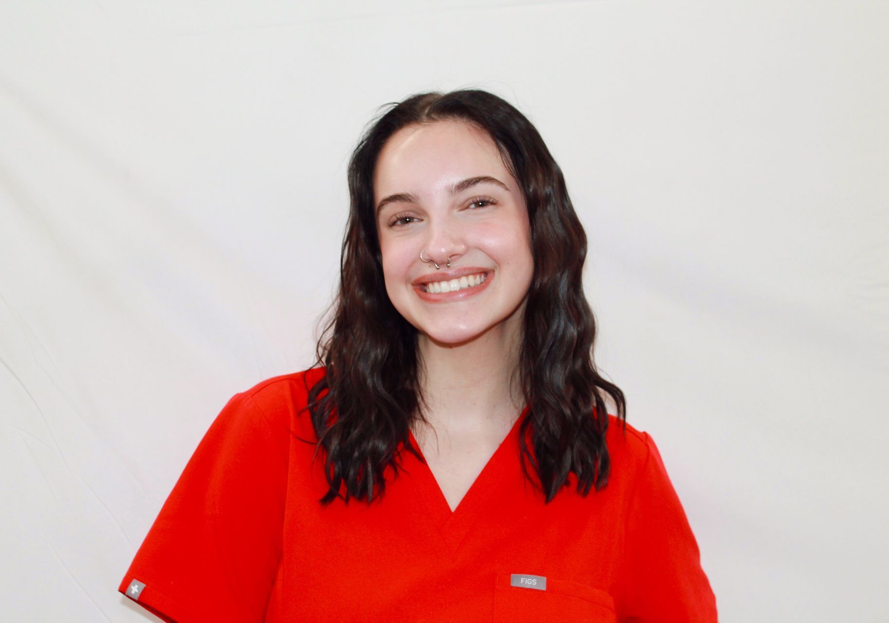 Katelyn Gardner with dark hair in red scrubs, wearing a nose ring, against a white background.