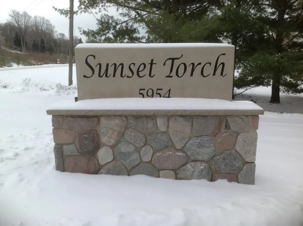 Sign for Sunset Torch at 5954, with a stone base and snowy ground.