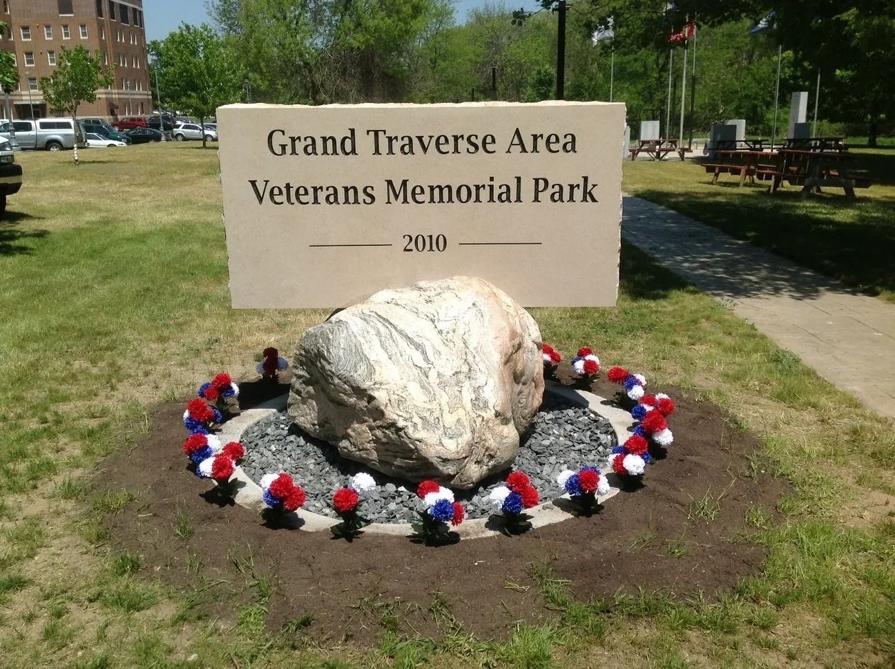 Grand Traverse Area Veterans Memorial Park sign with a rock and patriotic floral arrangement.