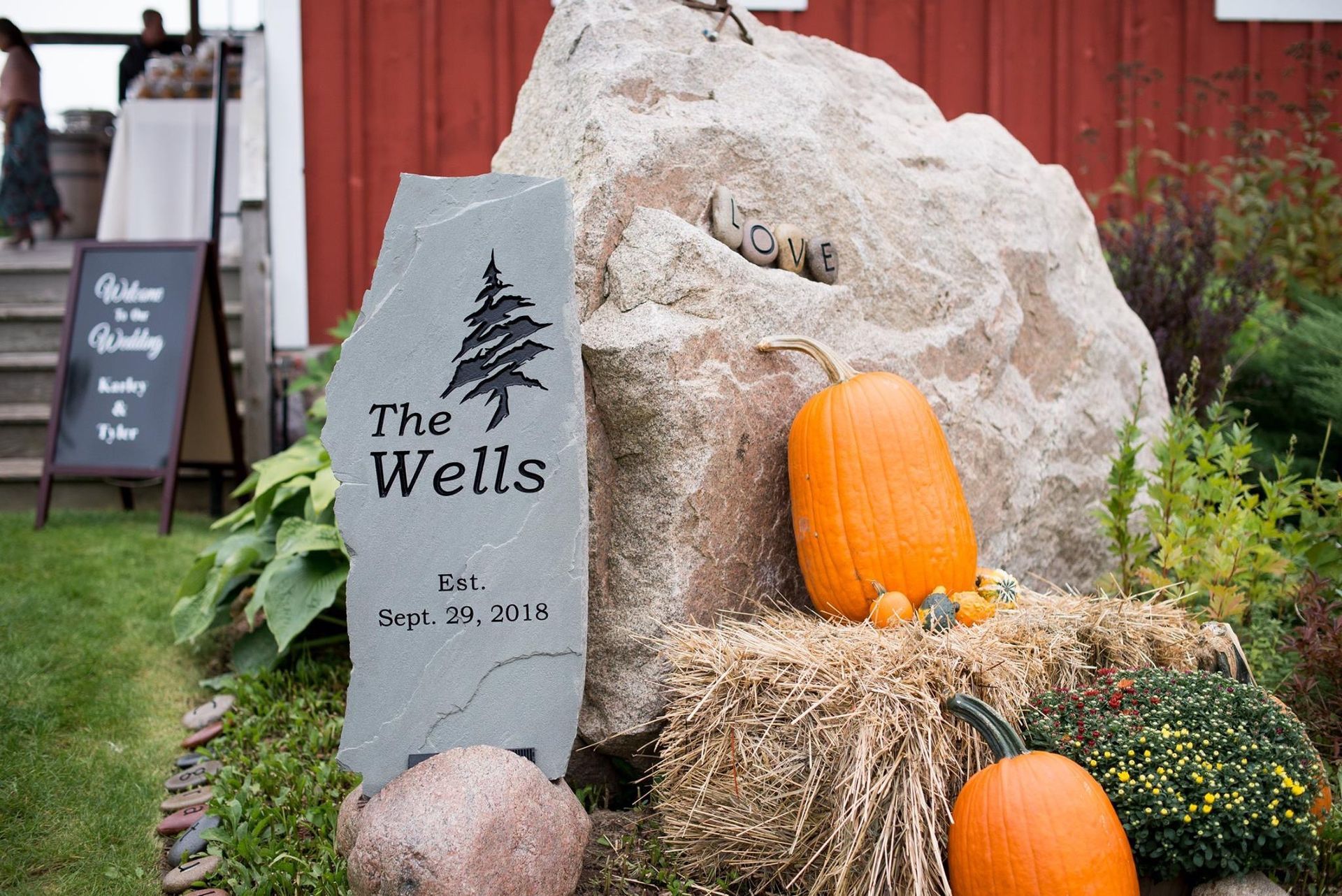 Wedding sign with pumpkins and hay bales in front of a large rock and red barn.