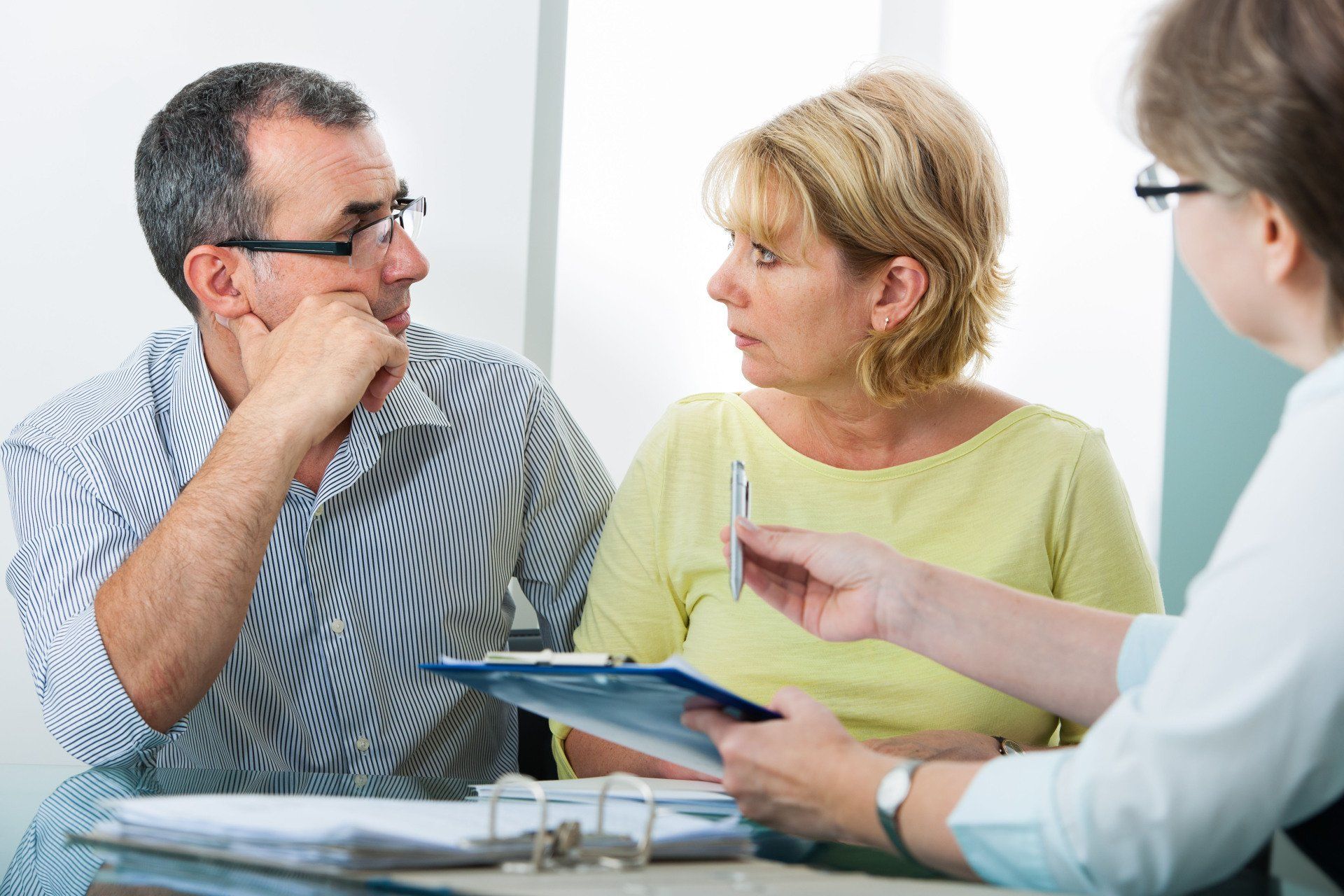 A couple consults with a person holding a clipboard and pen. The setting is indoors.