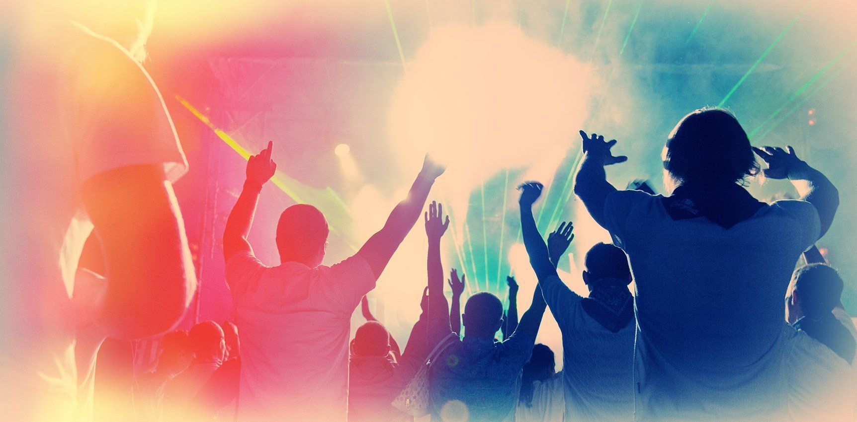 People with arms raised, silhouetted in a brightly lit, colorful concert setting.
