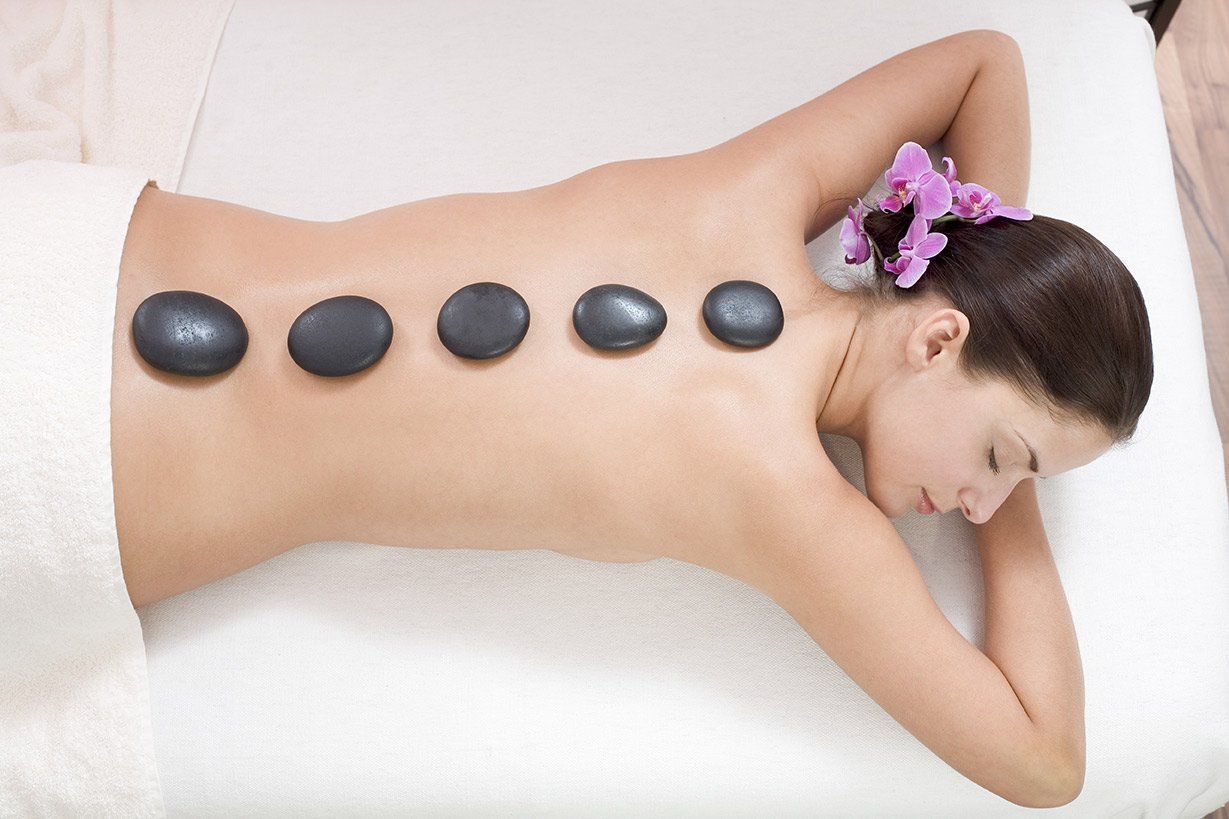 Woman receiving hot stone massage, face down, with stones on back.