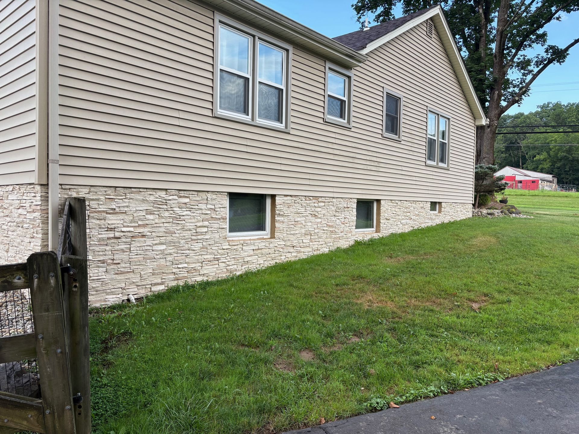 Tan and stone-clad house with green lawn, windows, and a partial view of a road.