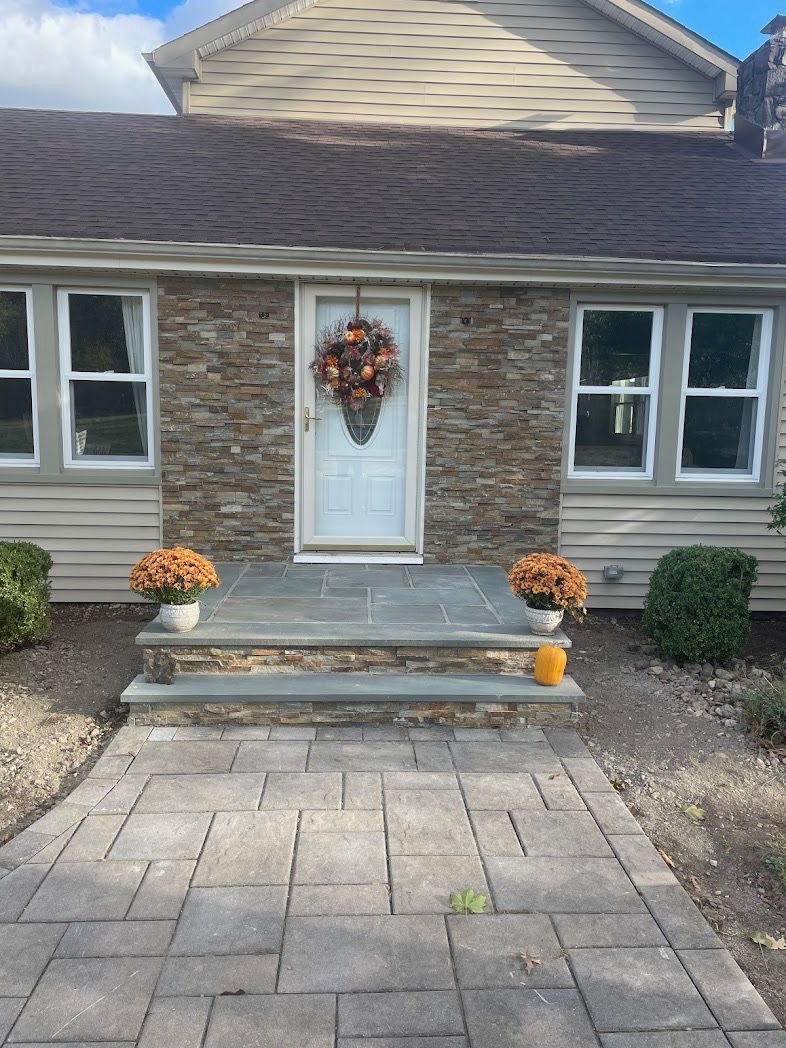 Stone facade entryway of a house with seasonal fall decorations; a wreath and orange flowers.