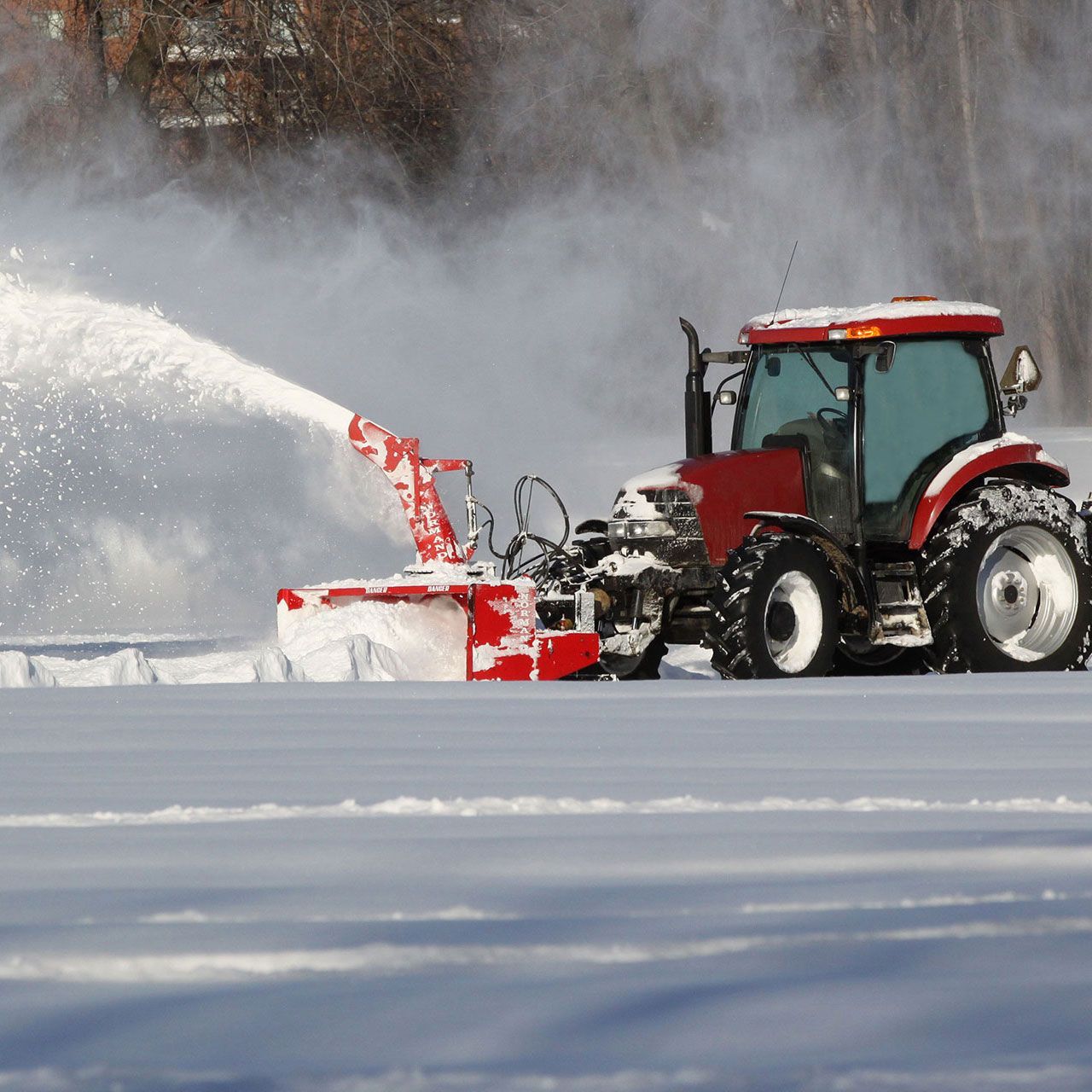 A red tractor is blowing snow in a snowy field.
