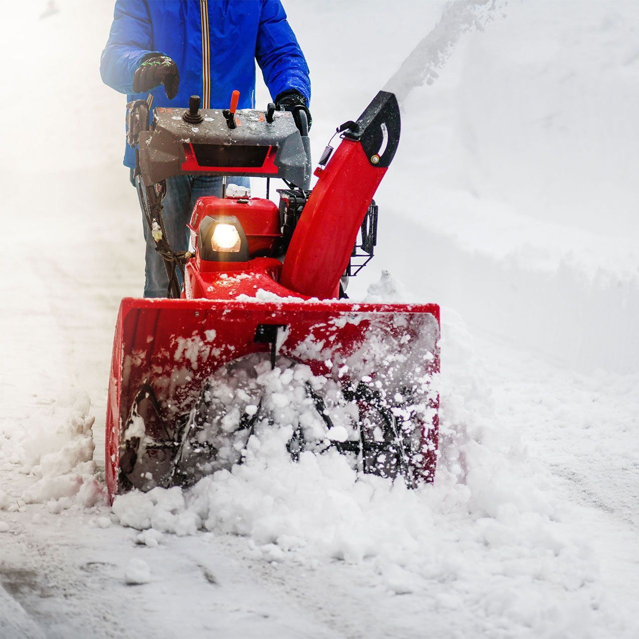 A man is using a snow blower to clear snow from a sidewalk.