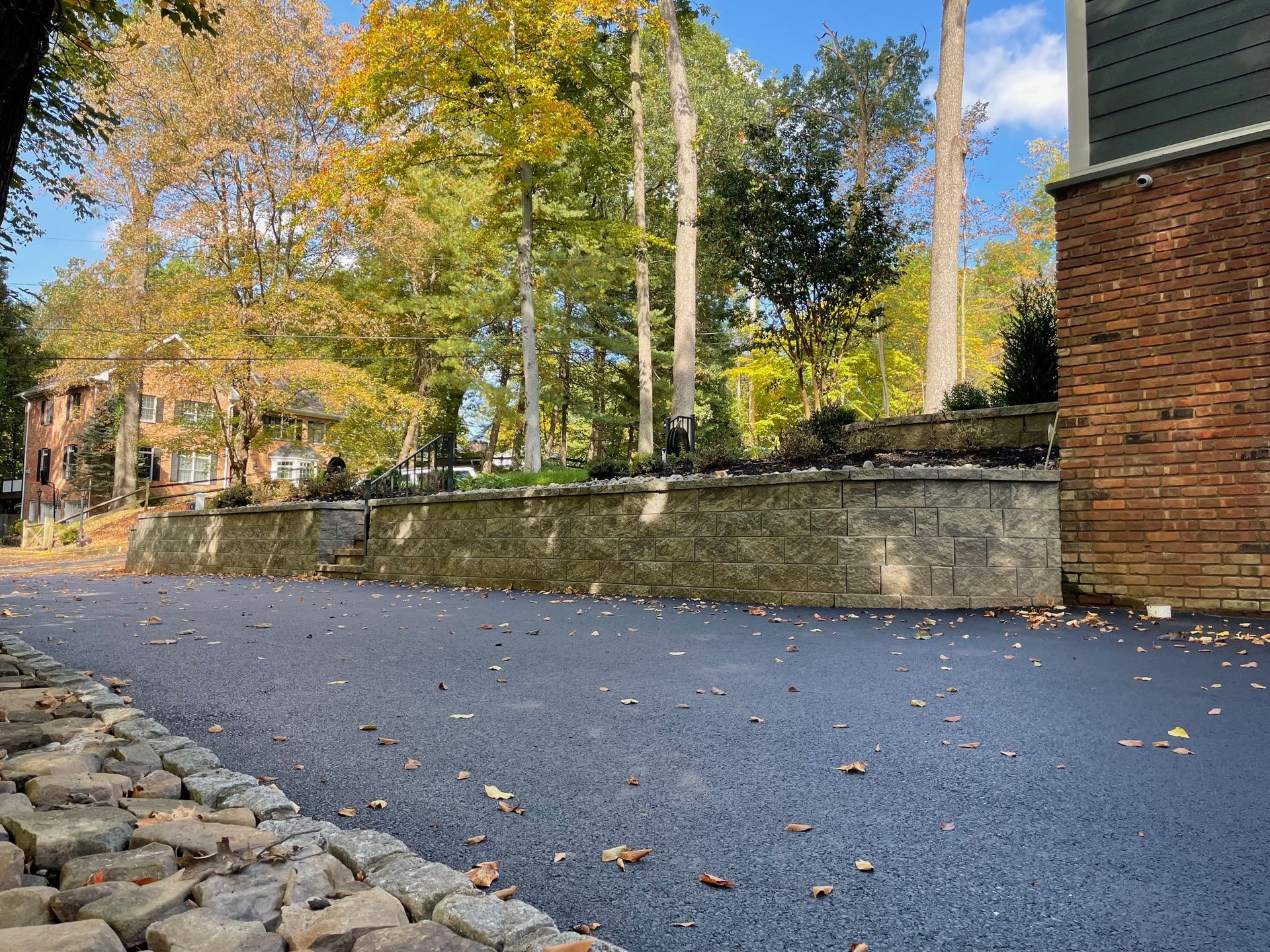 A paved driveway with a stone wall and trees.