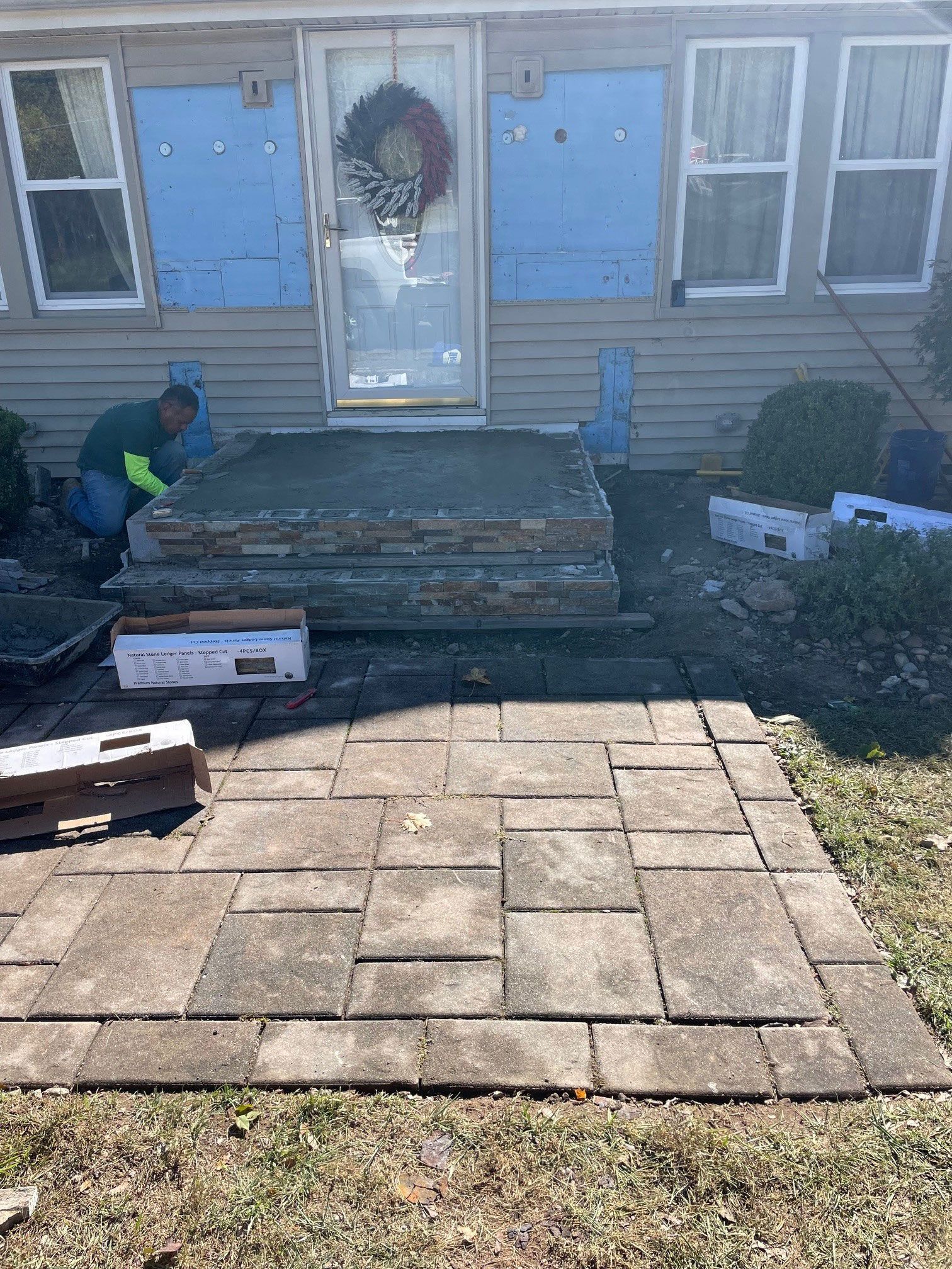 A man is working on a concrete porch in front of a house