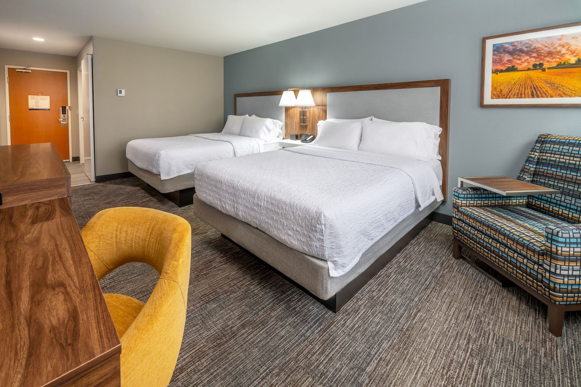 A hotel room with two beds , a chair , a desk and a picture on the wall.