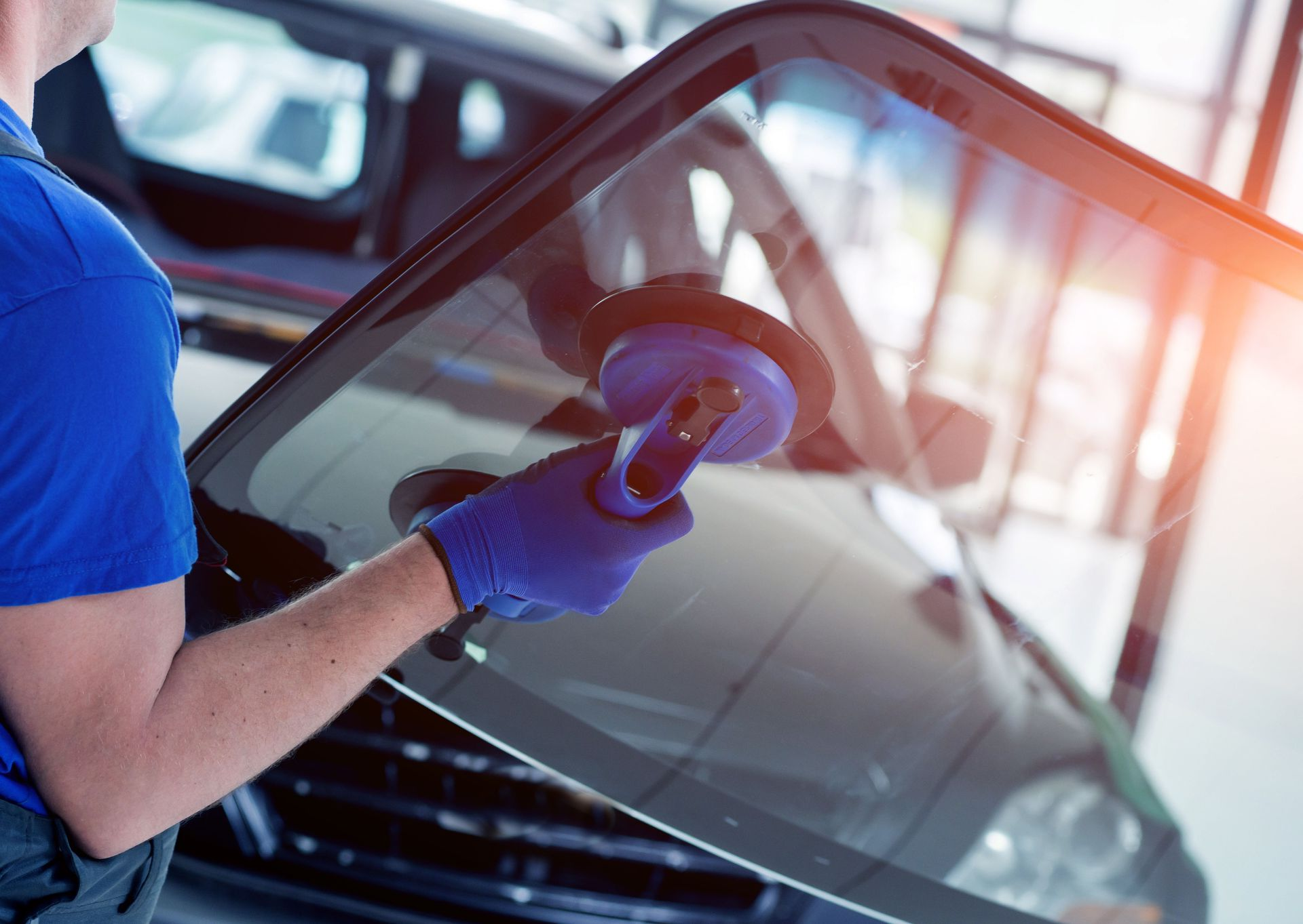 Person polishing a car windshield with a blue buffer in an auto shop