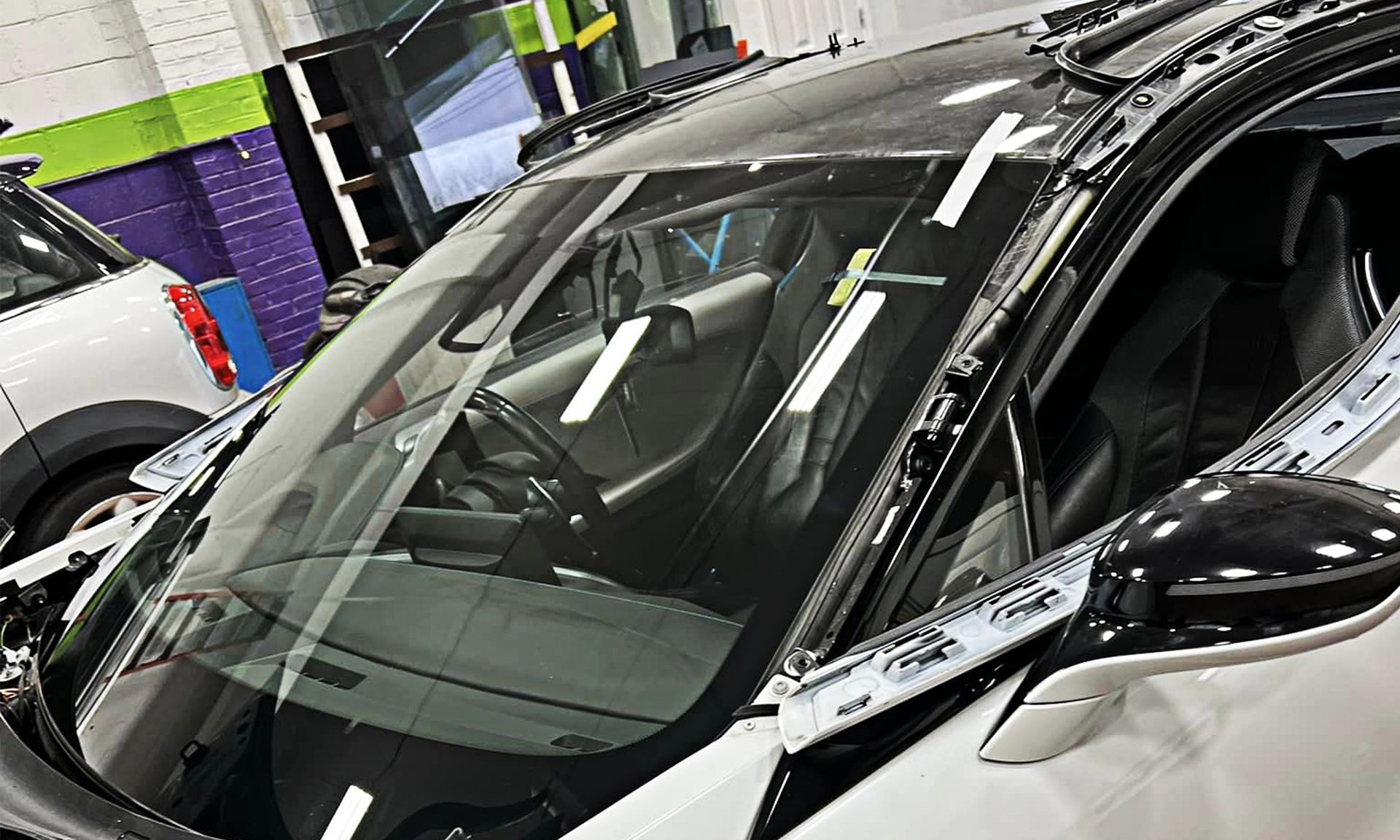 Black car in an auto shop with a windshield being worked on under bright lights