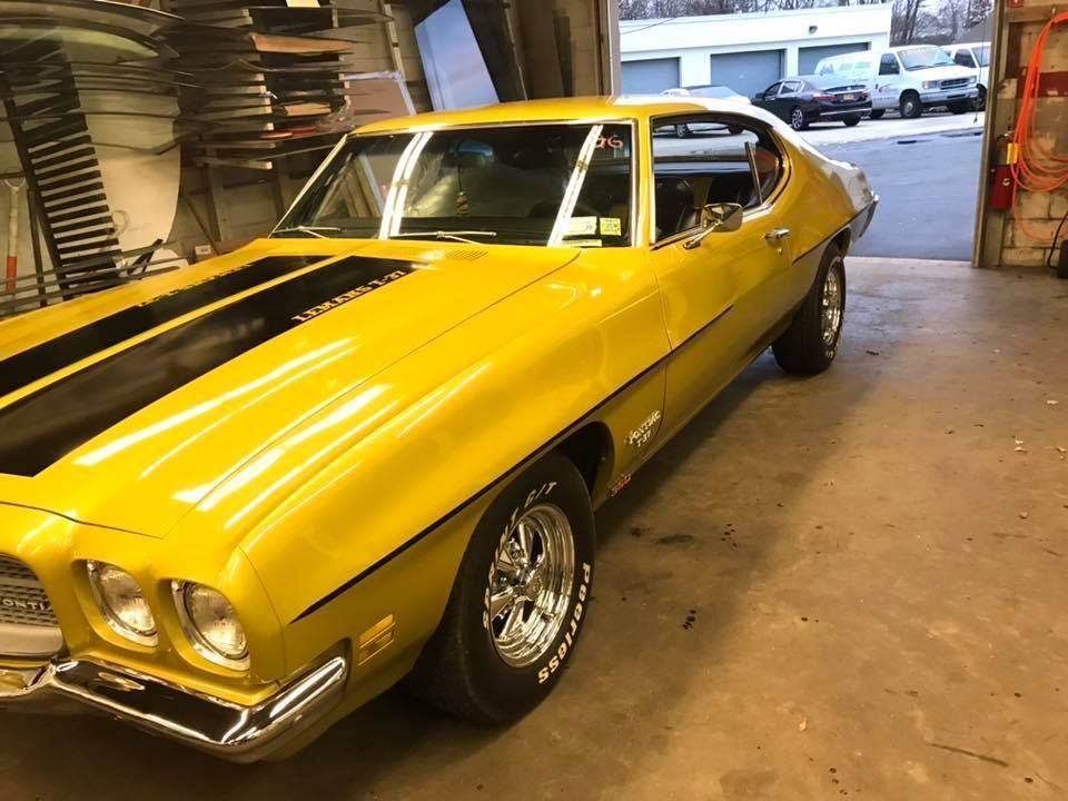 Yellow classic muscle car with black racing stripes parked in a garage doorway