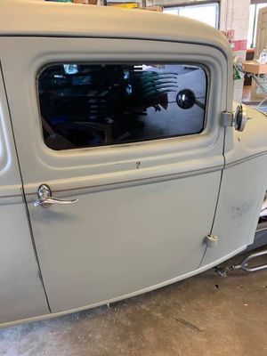 Cream-colored vintage car side view with a rounded window and chrome door handle in a garage.