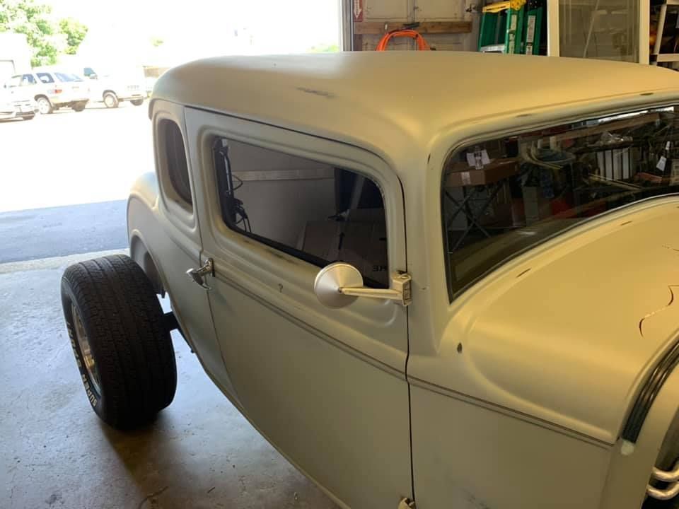 Classic cream-colored hot rod coupe in a garage, side view with exposed rear wheel.