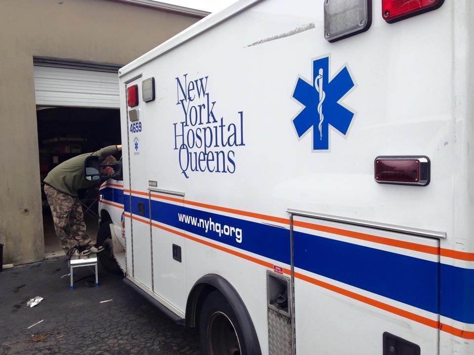 Paramedic loading gear into a New York Hospital Queens ambulance outside a garage