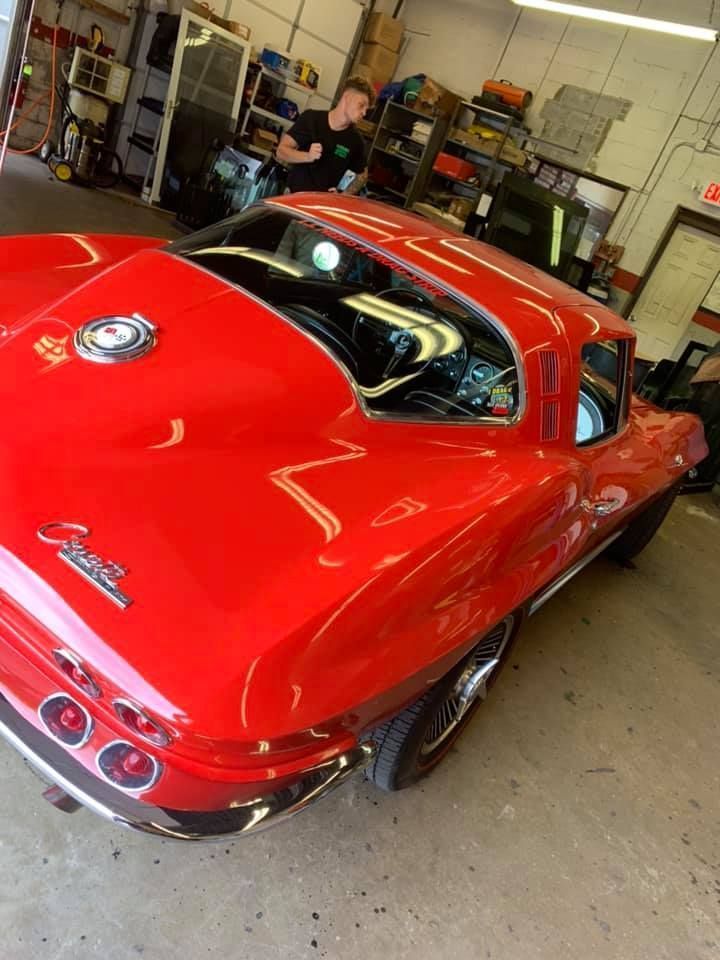 Red classic sports car in a garage, viewed from the rear-left.
