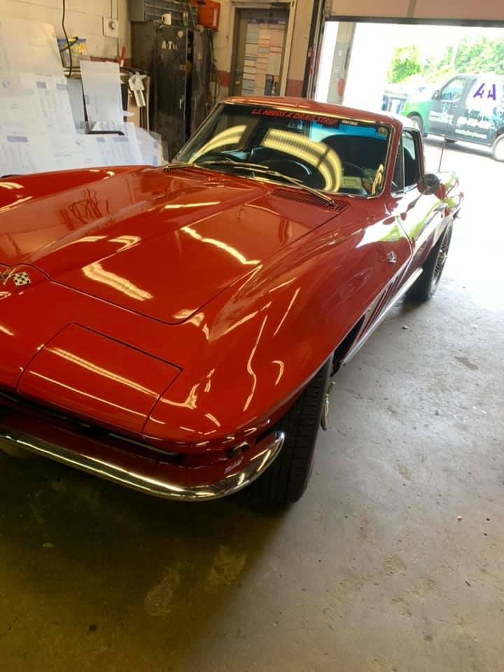 Red classic sports car parked in a garage, with a bright red hood and chrome bumper.