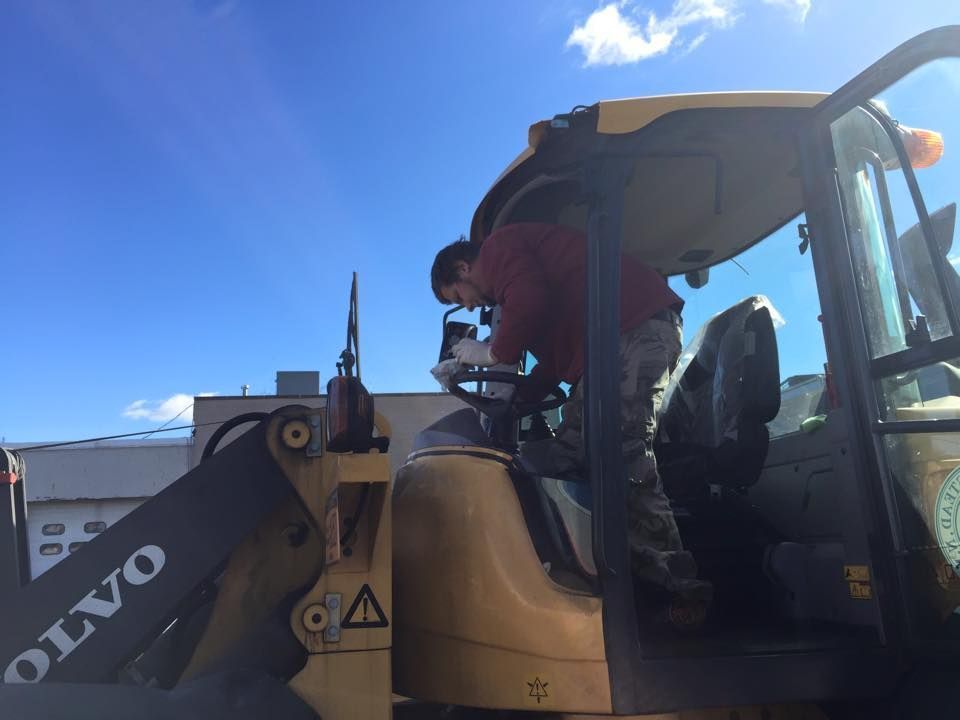 Construction worker in a yellow loader cab, with the bucket raised against a blue sky.