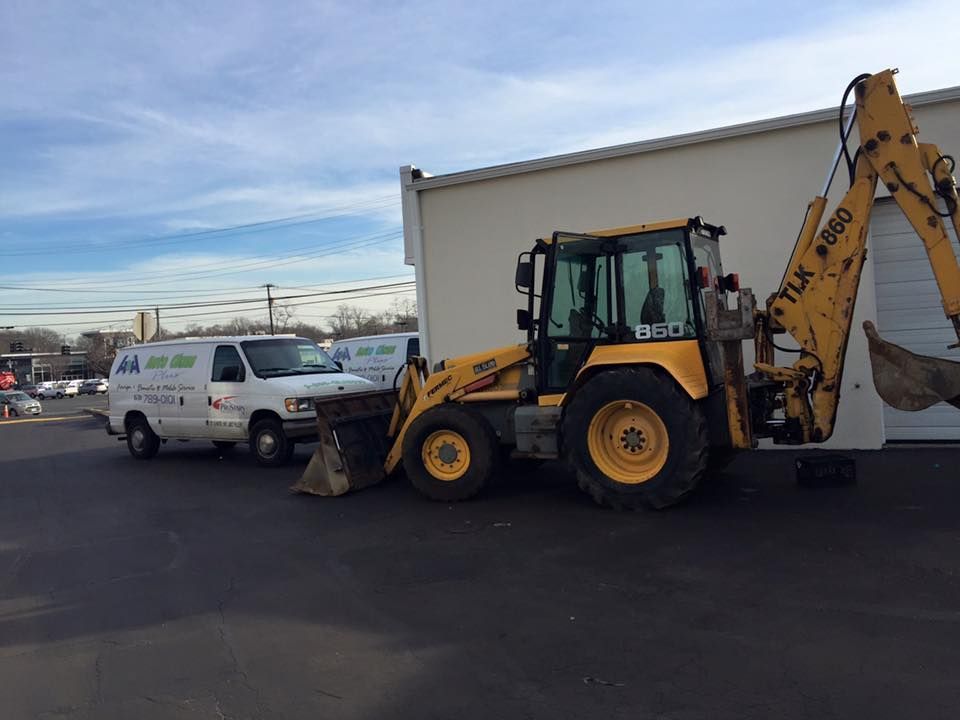 Yellow backhoe loader beside white work van in a parking lot under a cloudy sky.