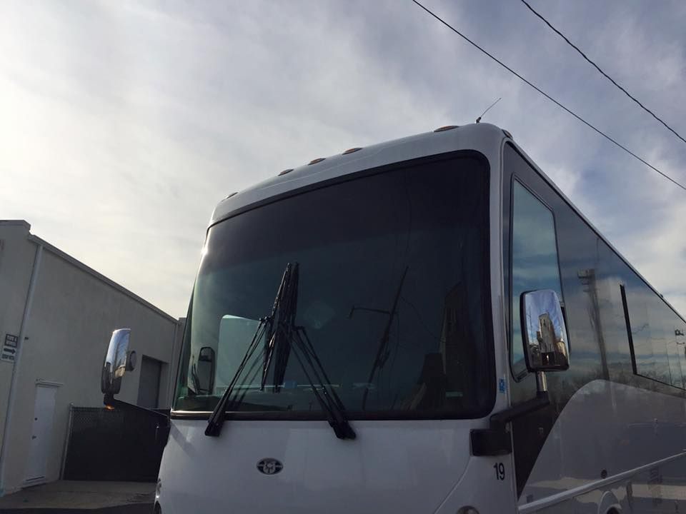 White tour bus parked outside a building under a cloudy sky, front view with windshield wipers visible
