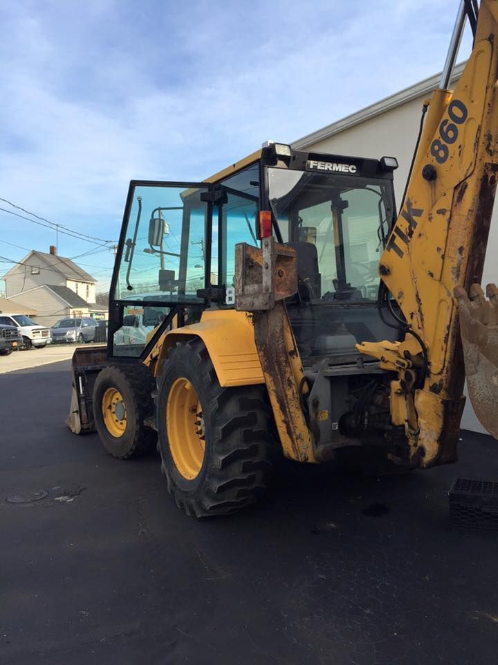 Yellow backhoe loader parked on a street beside houses on a sunny day