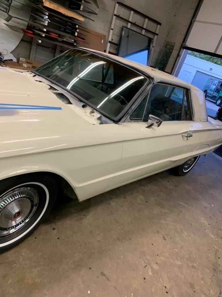 White classic car parked indoors in a garage, side view with chrome trim and vinyl roof