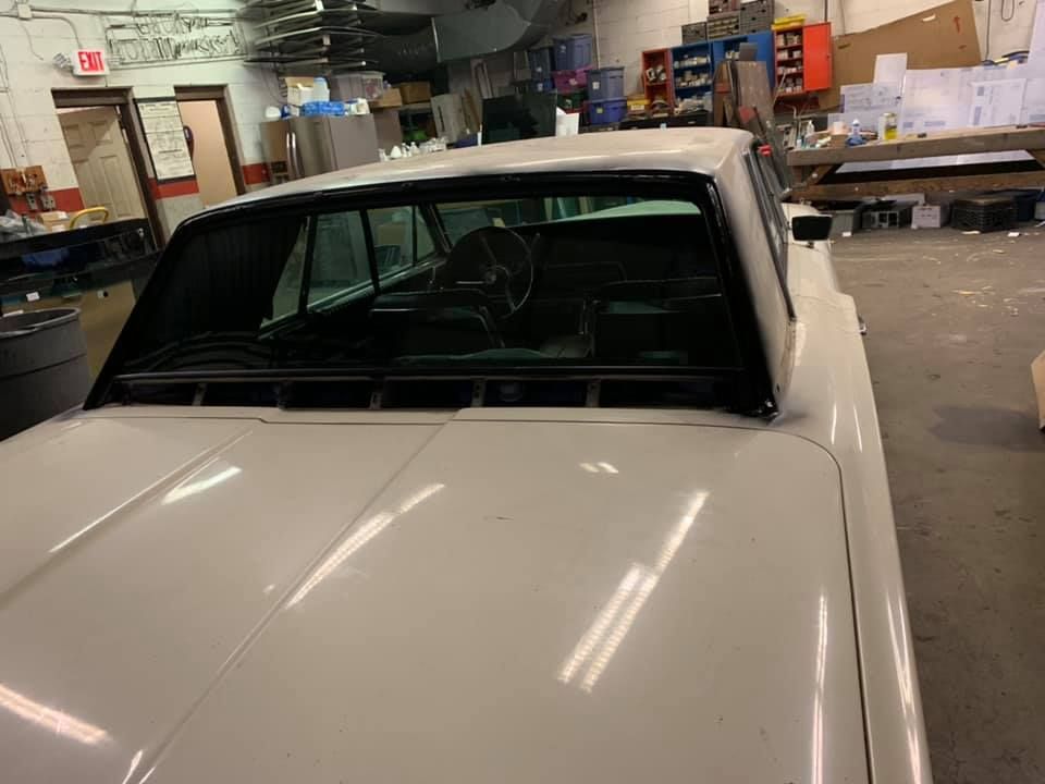 White vintage car inside an auto shop garage with tools and equipment in the background
