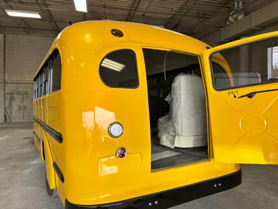 Yellow school bus with rear door open inside a warehouse, showing white seats inside
