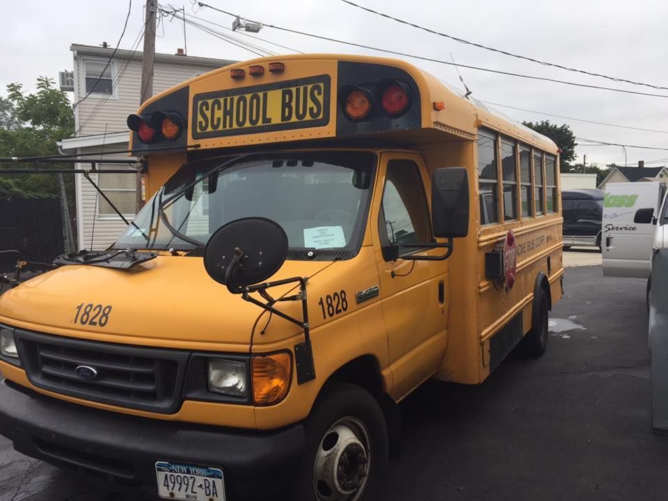 Yellow school bus parked in a lot, front view with “SCHOOL BUS” sign visible
