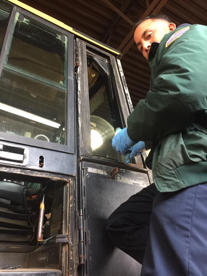 Worker in green jacket and blue gloves opening a bus door in a garage.