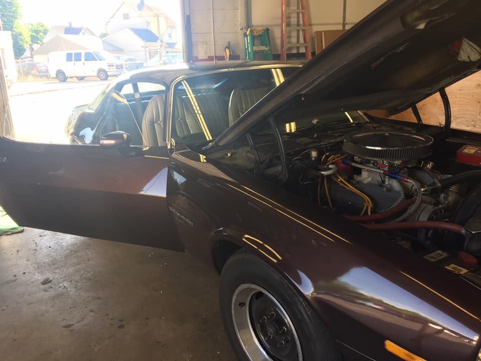 Classic maroon car in a garage with hood open and driver’s door ajar