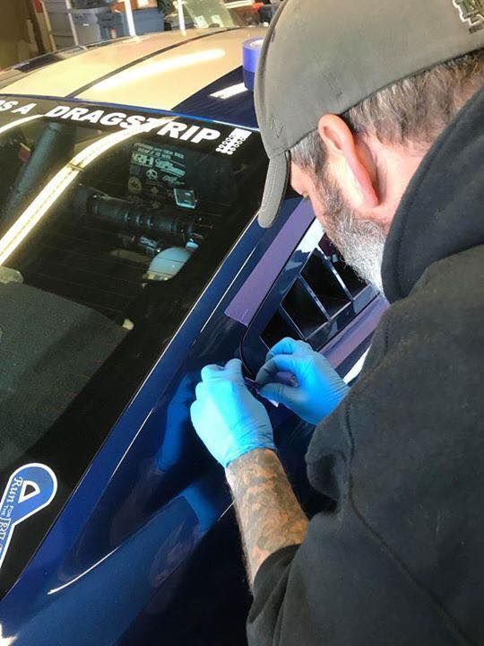 Technician in blue gloves inspects a blue race car window decal in a garage