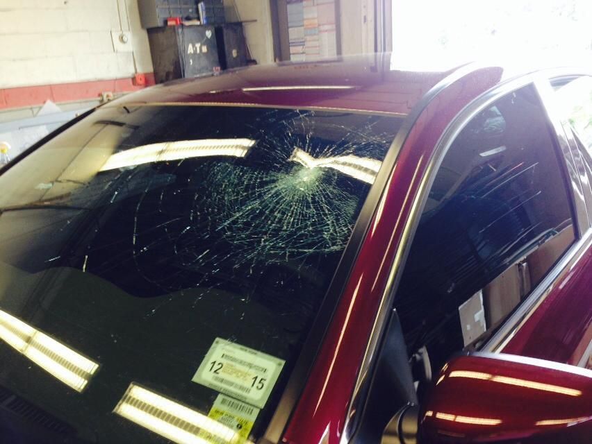 Red car windshield with a large shattered crack near the top center in a garage or auto shop.