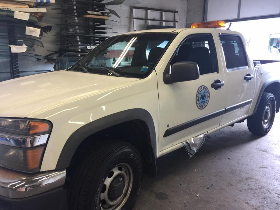 White utility pickup truck parked inside a garage or workshop with amber roof lights and a company logo on the door