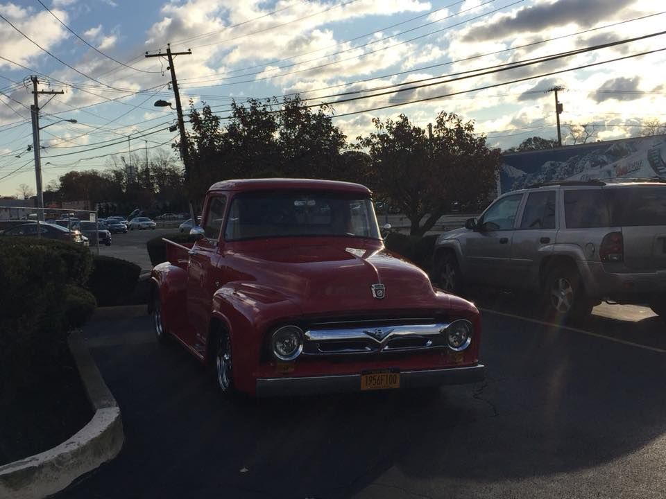 Red vintage pickup truck parked in a lot at sunset, with other vehicles and power lines in the background