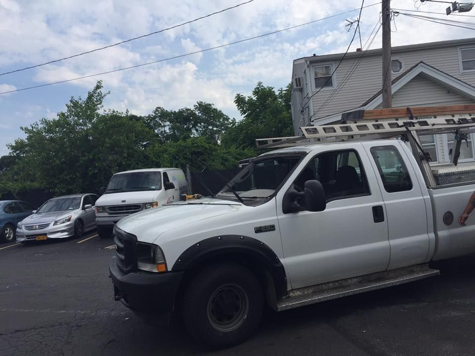 White work pickup truck parked in a lot beside a beige building and other cars under a cloudy sky