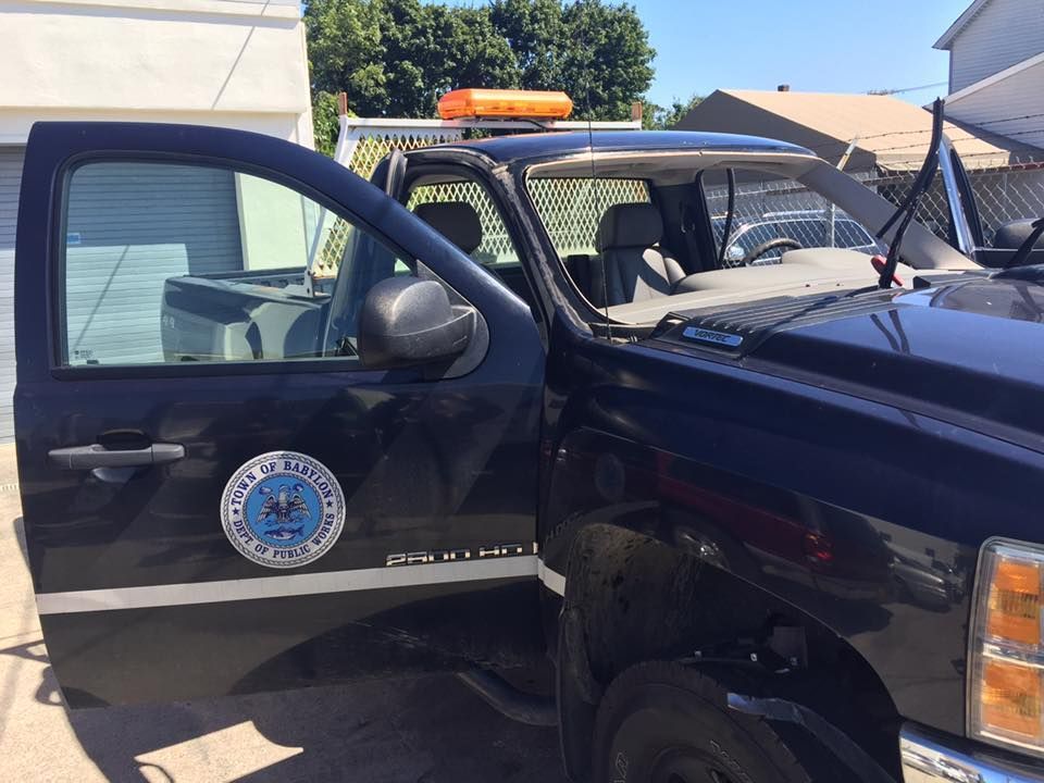Black police pickup truck with open driver door and light bar, parked outdoors in bright sun.