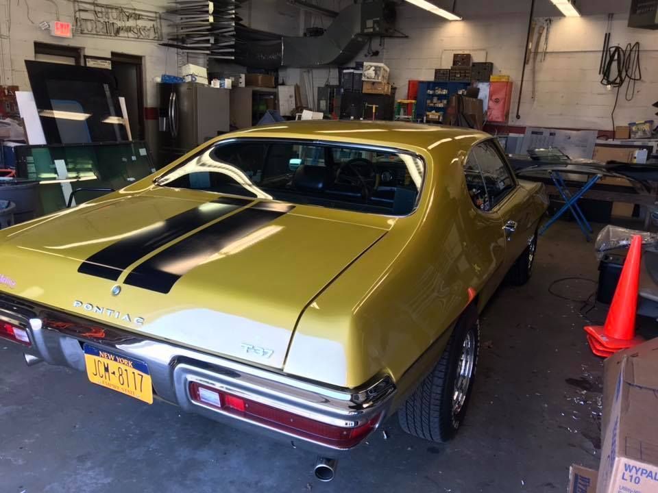 Yellow classic muscle car with black racing stripes parked in a garage workshop