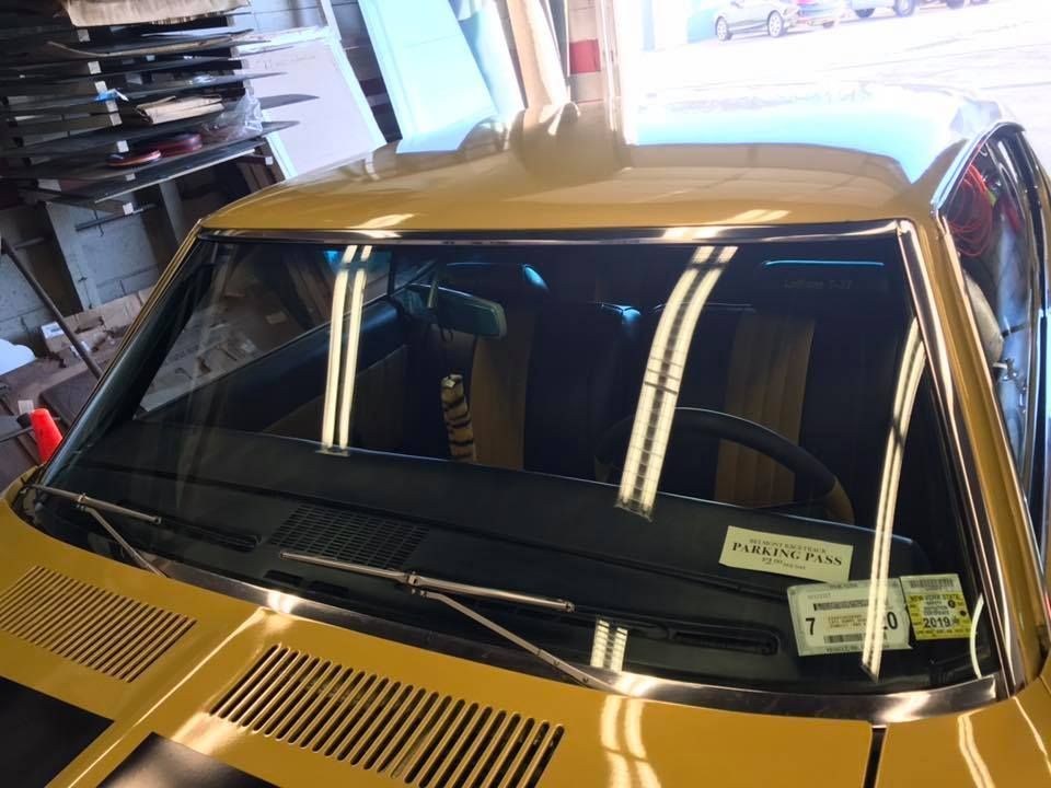 Yellow classic car windshield and hood in a garage, with reflections on the glass.