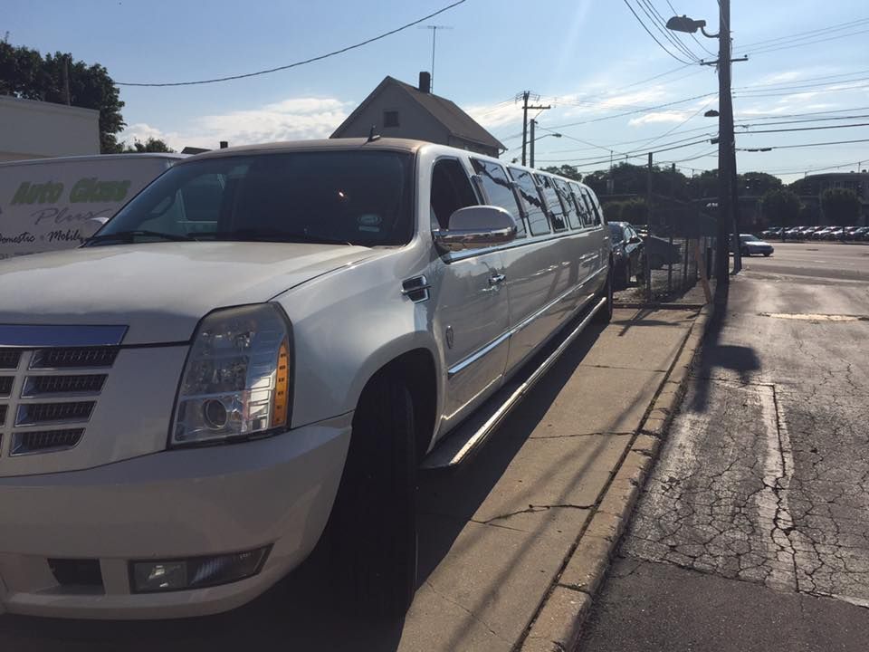 White stretch limousine parked on a sunny roadside beside a curb and sidewalk.