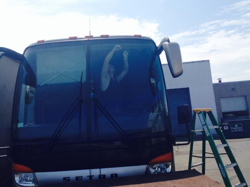 White bus parked outside a building with a green ladder leaning beside it.