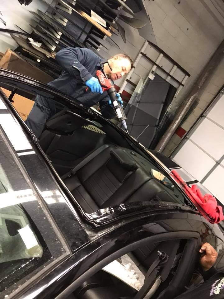 Mechanic polishing a black car in a garage, with another person leaning into the passenger side.