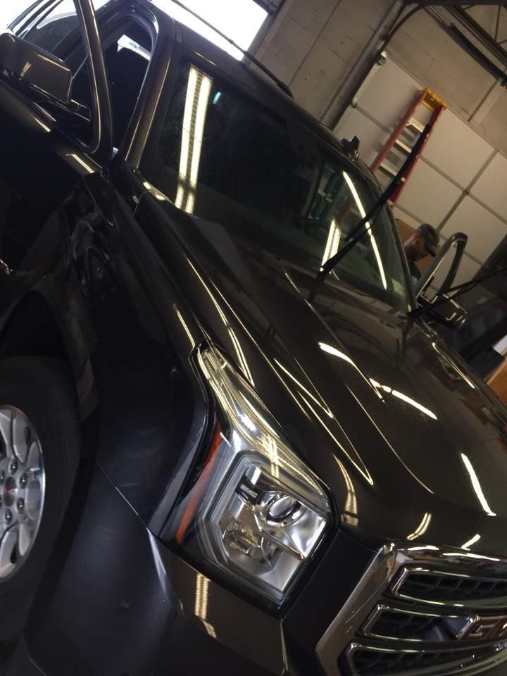 Black SUV in a garage, viewed from the front-left with overhead lights reflected on the hood.