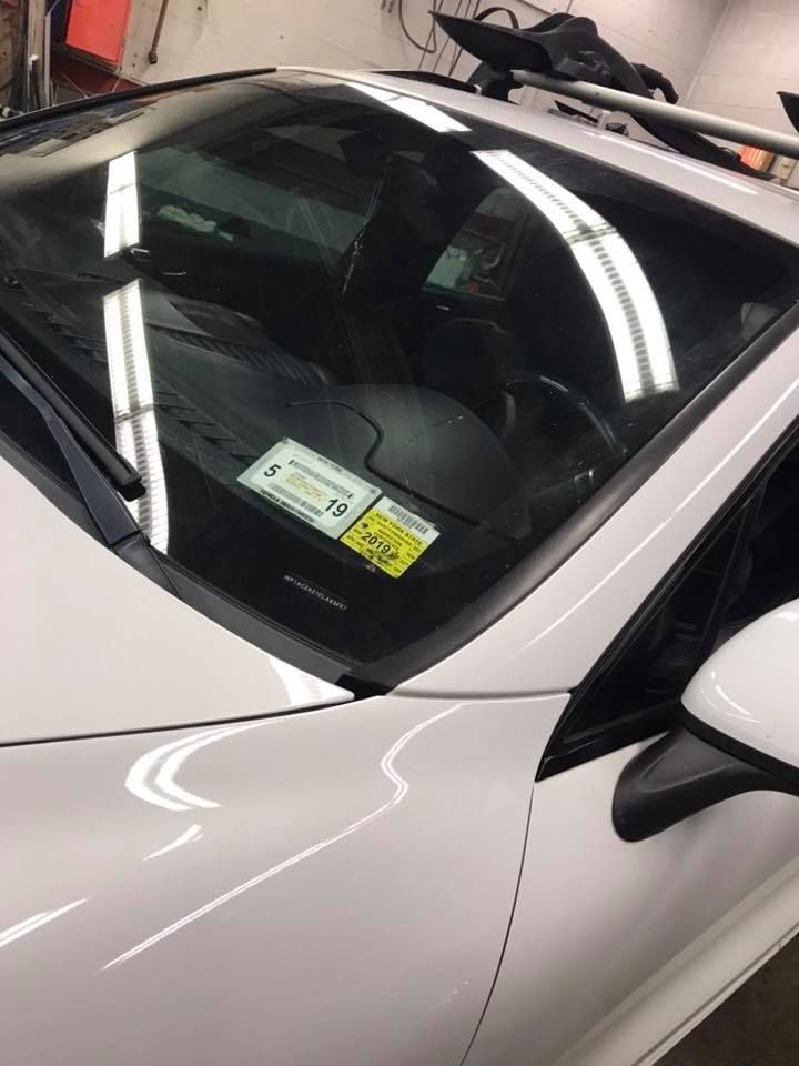 White car windshield with inspection stickers in a garage or showroom.