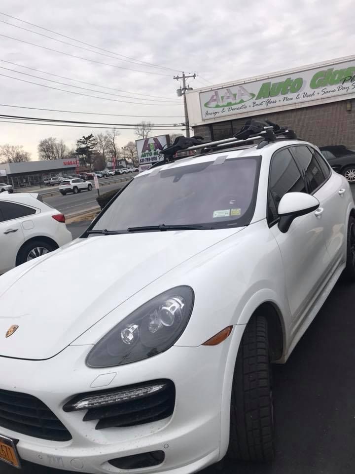 White Porsche SUV parked in a lot, front view with tilted wheels and a store sign in the background