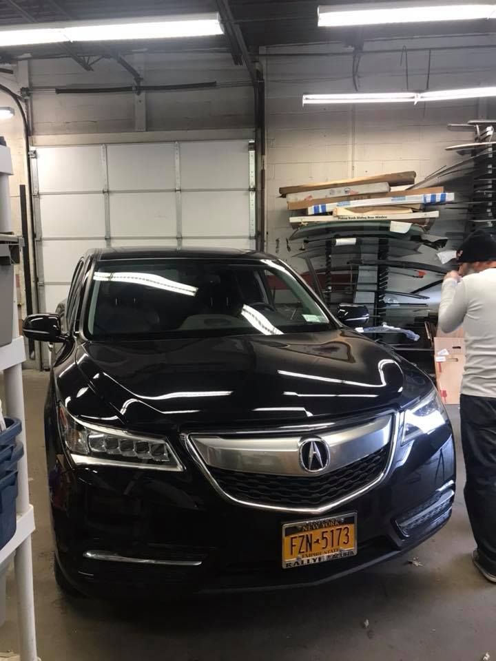 Black Acura SUV in a garage with a person standing beside it near shelves of materials
