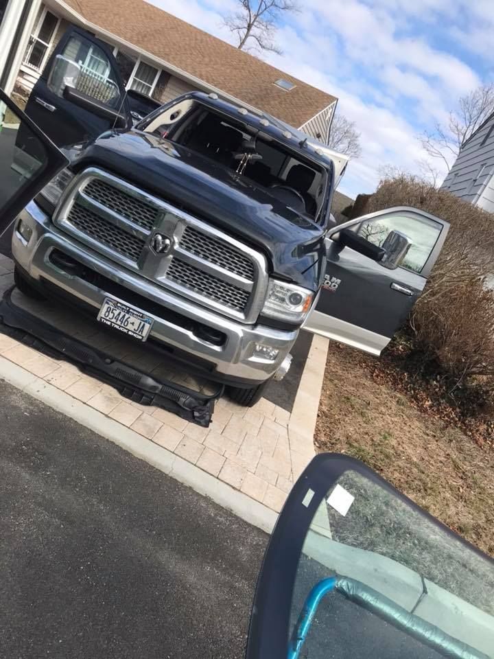 Black pickup truck parked in a driveway with driver door open, viewed from inside a car window